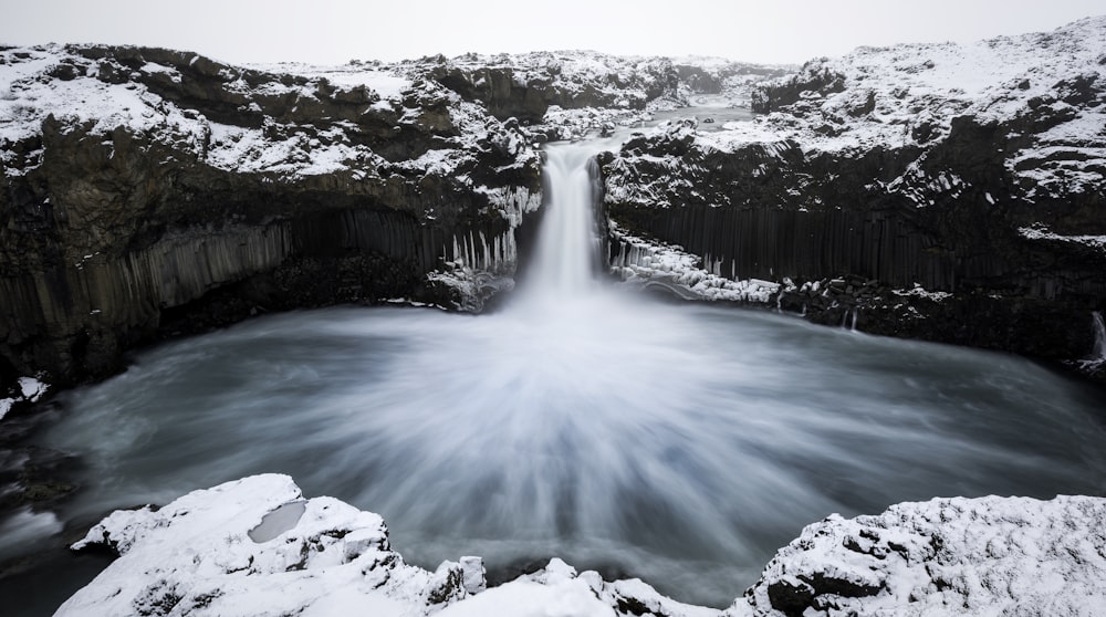 a large waterfall is surrounded by snow covered rocks