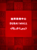 A brightly illuminated red sign featuring the words 'Dubai Mall' in English, Chinese, and Arabic. Surrounding the central text are various Chinese characters embossed into the red background.