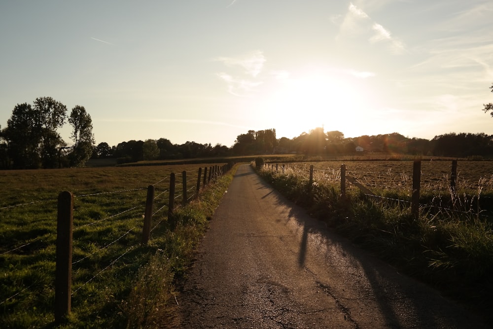 the sun is setting over a field with a fence