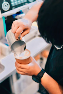 A skilled barista pouring latte art into a ceramic cup inside a modern, elegant coffee shop