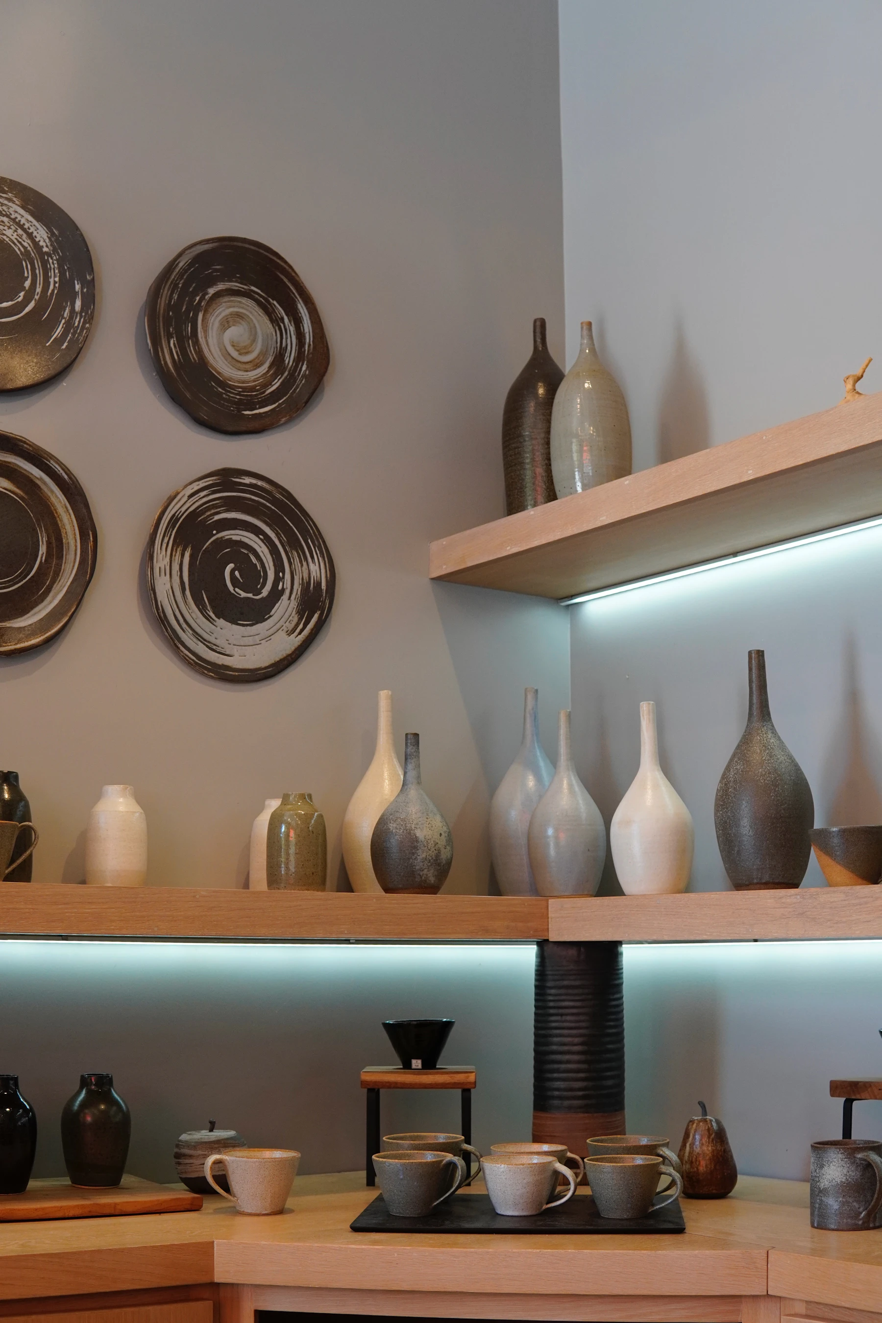 Stoneware vases, cups and swirl-glazed plates displayed on lit wooden shelves