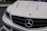 The image features the front portion of a white luxury car, prominently displaying the emblem on the hood. The sleek design includes distinctive headlight styling and a black grille adding contrast to the white exterior.