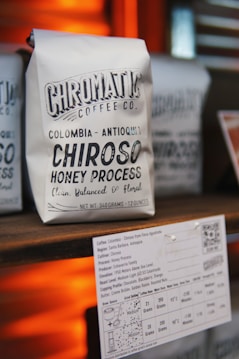A close-up of a coffee package labeled 'Chromatic Coffee Co.' featuring a variety named 'Chiroso Honey Process' from Colombia. The packaging highlights traits like 'clean, balanced, & floral' and provides a weight specification of 12 ounces. Below it, there is a detailed coffee information card indicating origin, process, tasting notes, and other specifics.