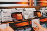 Several neatly arranged bags of coffee from Chromatic Coffee Co. are displayed on a wooden shelf. Each bag has detailed labeling with names like 'Côtes du Rhône' and 'Bourbogne,' suggesting different blends or origins. A hand is holding a card with additional information about the coffee.