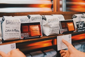 Several neatly arranged bags of coffee from Chromatic Coffee Co. are displayed on a wooden shelf. Each bag has detailed labeling with names like 'Côtes du Rhône' and 'Bourbogne,' suggesting different blends or origins. A hand is holding a card with additional information about the coffee.