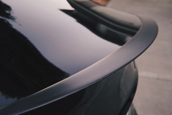 Close-up shot of a sleek black car spoiler installed on a sports car under bright sunlight.