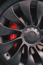 A sleek black and silver premium car rim showcased on a glossy red background.