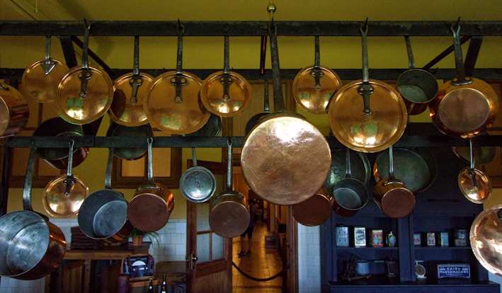 A sturdy ceiling-mounted pot rack holding various copper pots and pans above a rustic kitchen island