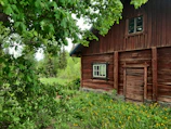 Rustic wooden cabin surrounded by lush greenery and a small garden with wildflowers.