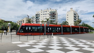 a red and black train traveling past tall buildings