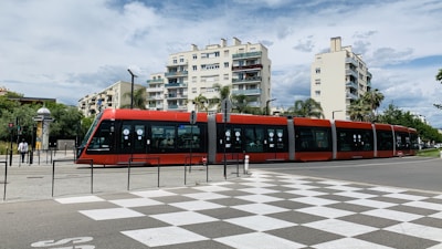 a red and black train traveling past tall buildings