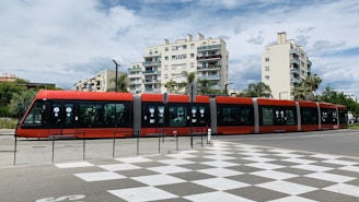a red and black train traveling past tall buildings