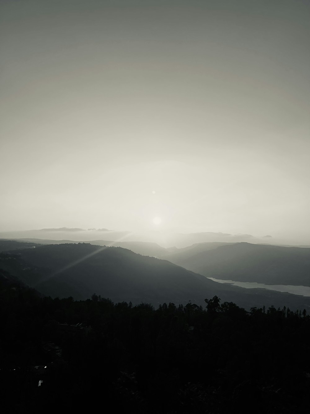 a black and white photo of the sun setting over mountains