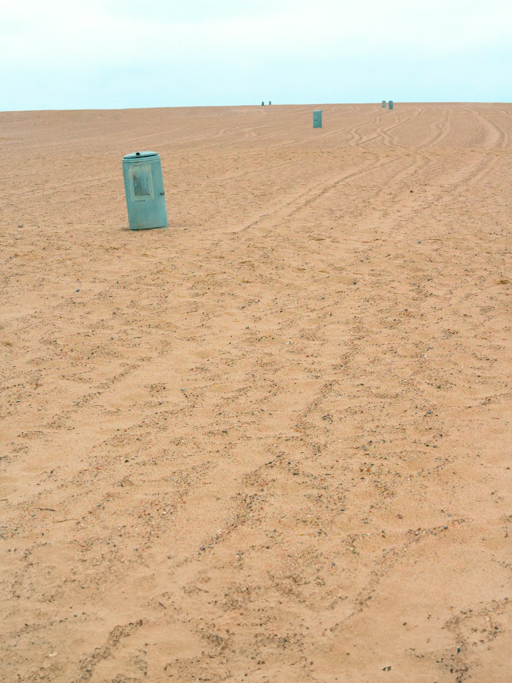 a blue trash can sitting in the middle of a desert