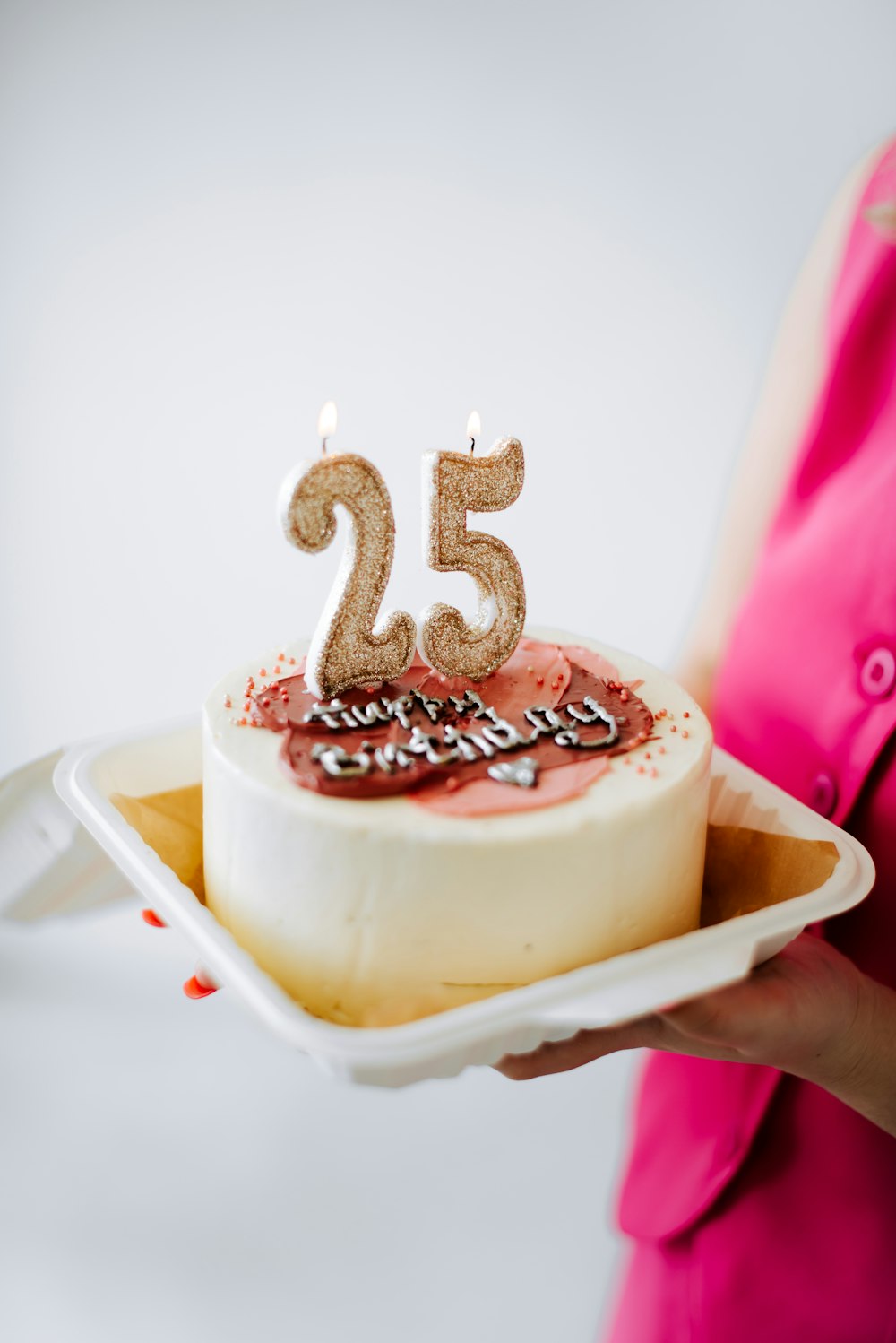 a woman holding a cake with a candle in the shape of the number twenty five