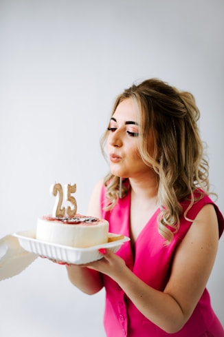 a woman in a pink dress holding a cake with the number twenty five on it