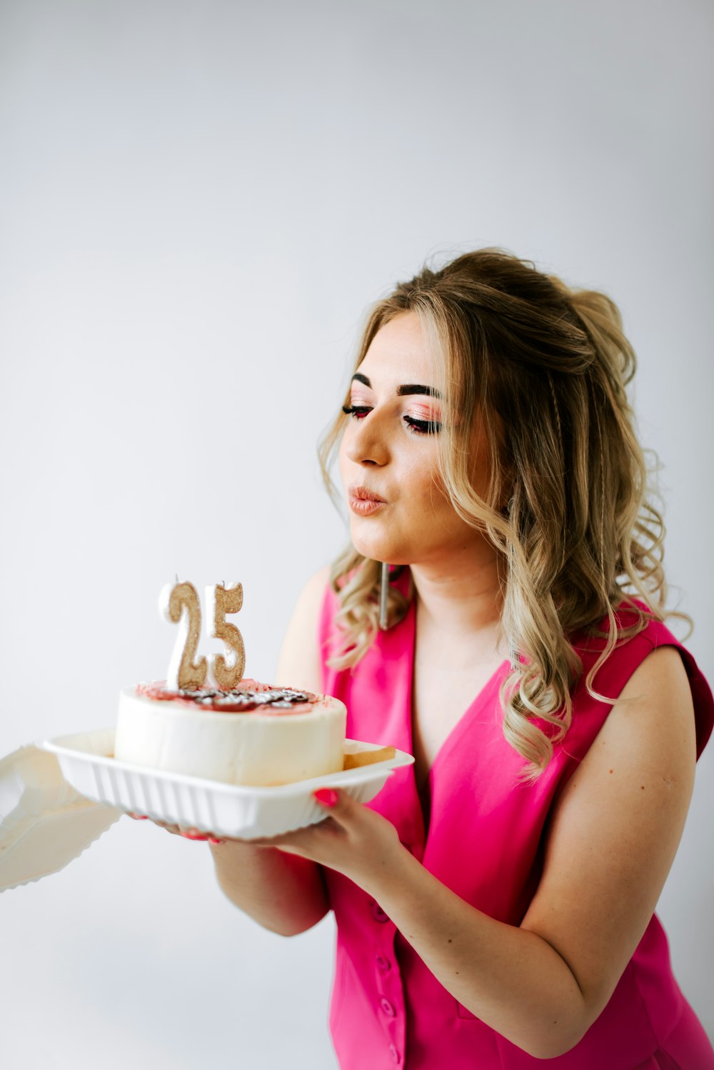 a woman in a pink dress holding a cake with the number twenty five on it