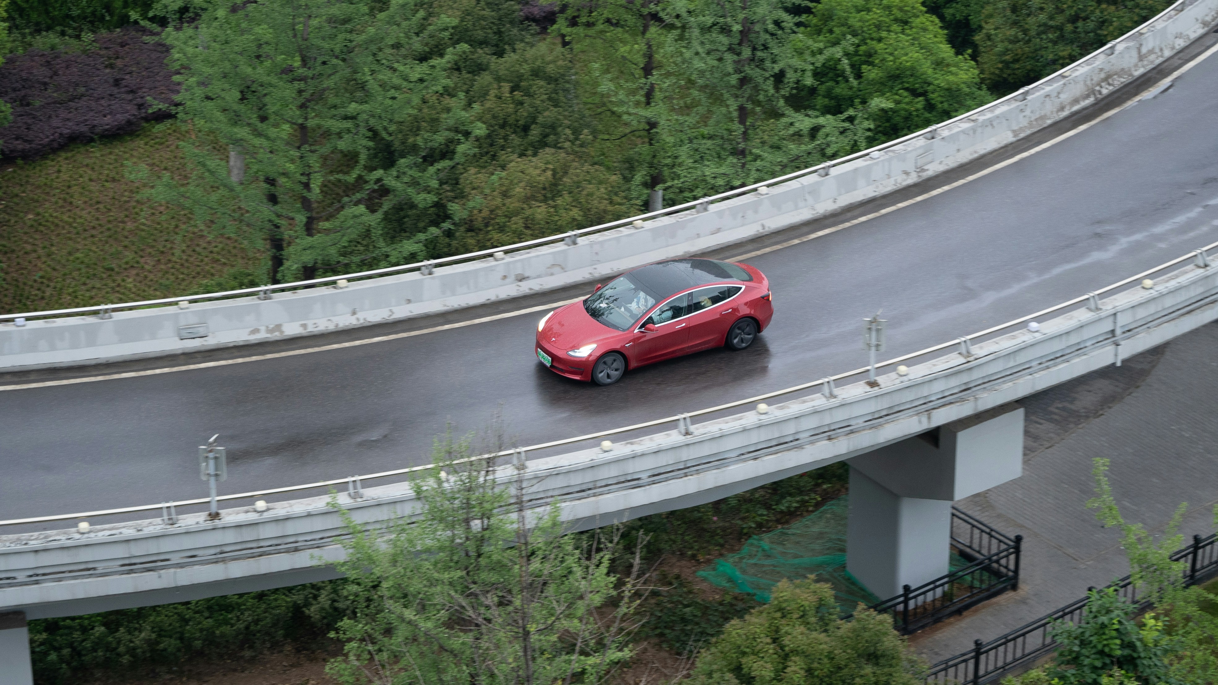 a red car driving down a road next to a bridge