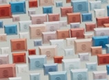 A pattern of rectangular 3D shapes in various sizes and colors, including blue, red, beige, and white, featuring globe emblems on each. The shapes are arranged in a scattered, overlapping design on a light background.