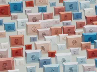 A pattern of rectangular 3D shapes in various sizes and colors, including blue, red, beige, and white, featuring globe emblems on each. The shapes are arranged in a scattered, overlapping design on a light background.