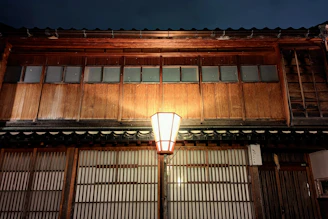A delicate handcrafted miniature Japanese house glowing softly under warm amber lantern light.
