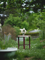 A small, rustic outdoor accent stool beside a blooming garden, perfect for resting a drink.