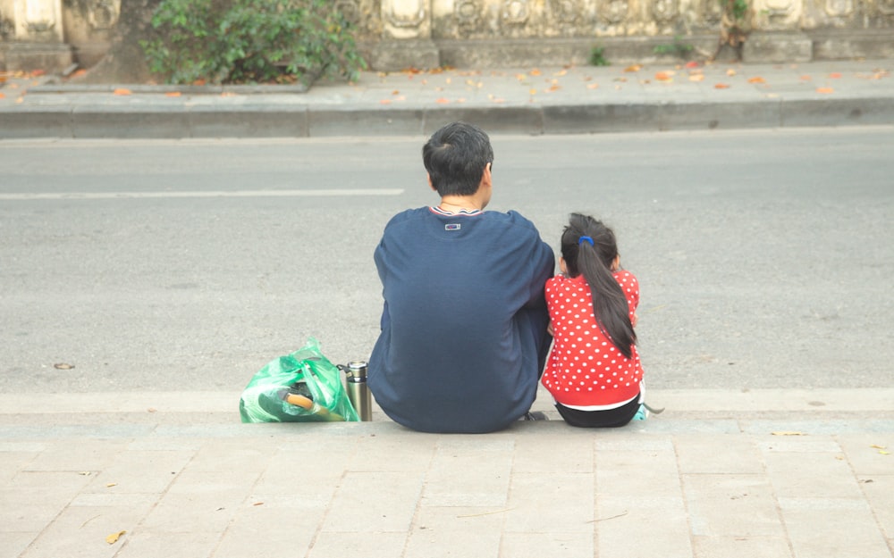 a man and a little girl sitting on the sidewalk