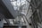 A modern architectural interior featuring large metal and glass structures, creating an intricate network of beams and walkways. The design is sleek and futuristic, with ample natural light pouring in through the windows lining the walls and ceiling.