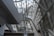 A modern architectural interior featuring large metal and glass structures, creating an intricate network of beams and walkways. The design is sleek and futuristic, with ample natural light pouring in through the windows lining the walls and ceiling.