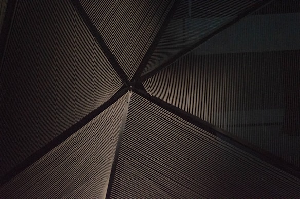 Lines converge at a central point, creating a geometric and symmetrical pattern. The scene appears to be an abstract architectural detail, possibly a ceiling or a wall, with a textured, metallic surface.
