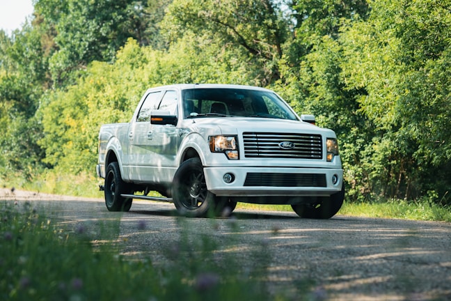 A freshly replaced windshield gleaming under the sun on a white pickup truck parked at a local park.