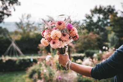 A gentle scene of a woman in a flowing peach dress holding a bouquet of lavender and pink flowers in a sunlit garden.