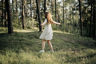 A young woman twirling in a breezy skirt with a backdrop of sunlit trees.