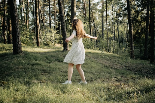 Emy twirling joyfully in a flowing red dress, sunlight filtering through garden leaves.