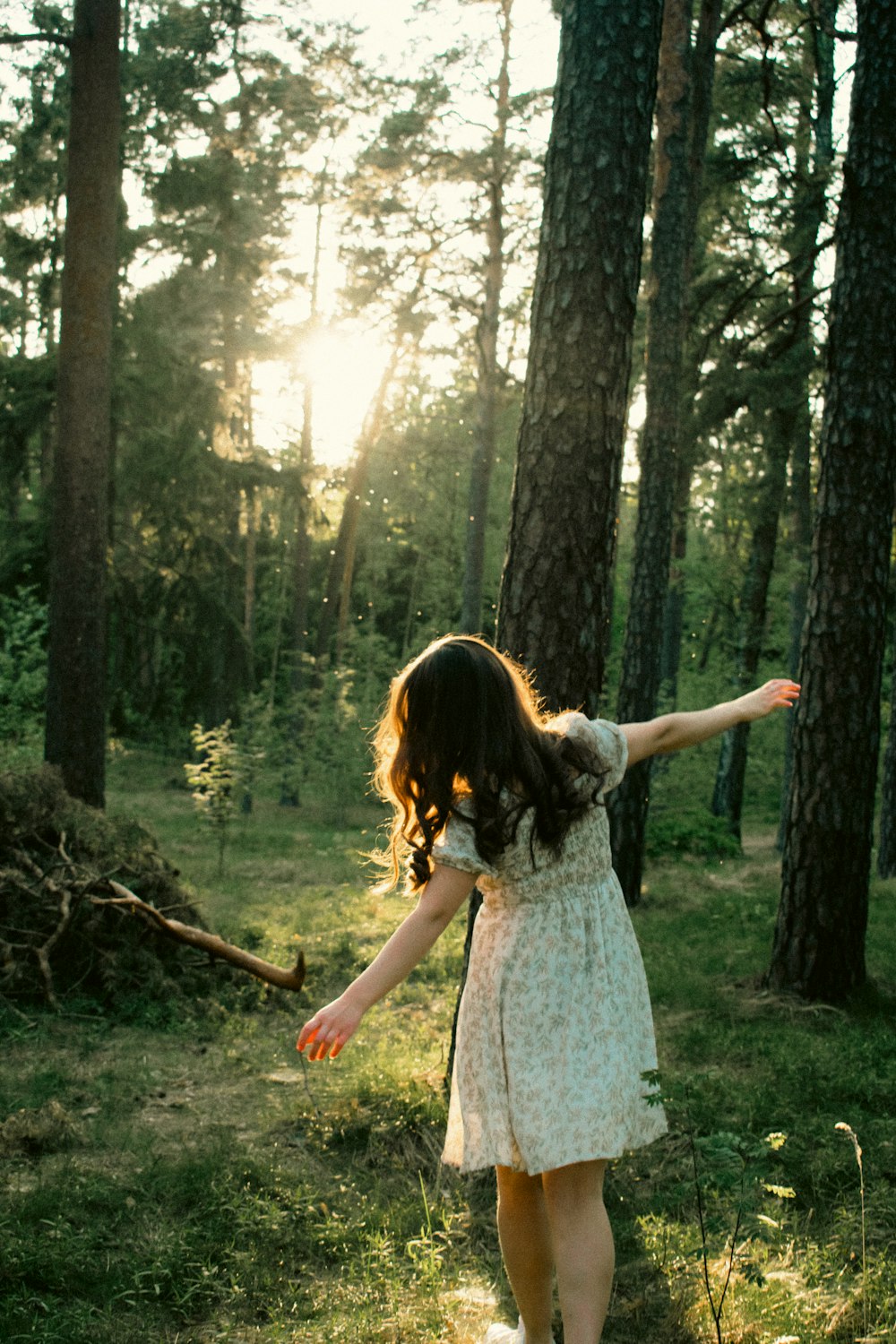 a girl in a dress is walking through the woods