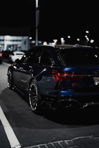 A sleek black luxury sedan parked under soft city lights at dusk.