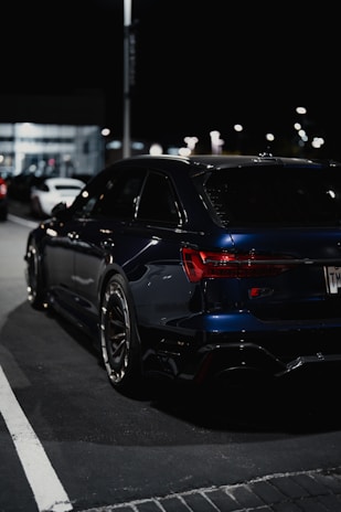 Elegant black car parked beside a trendy event venue at night with soft reflections on the paint.