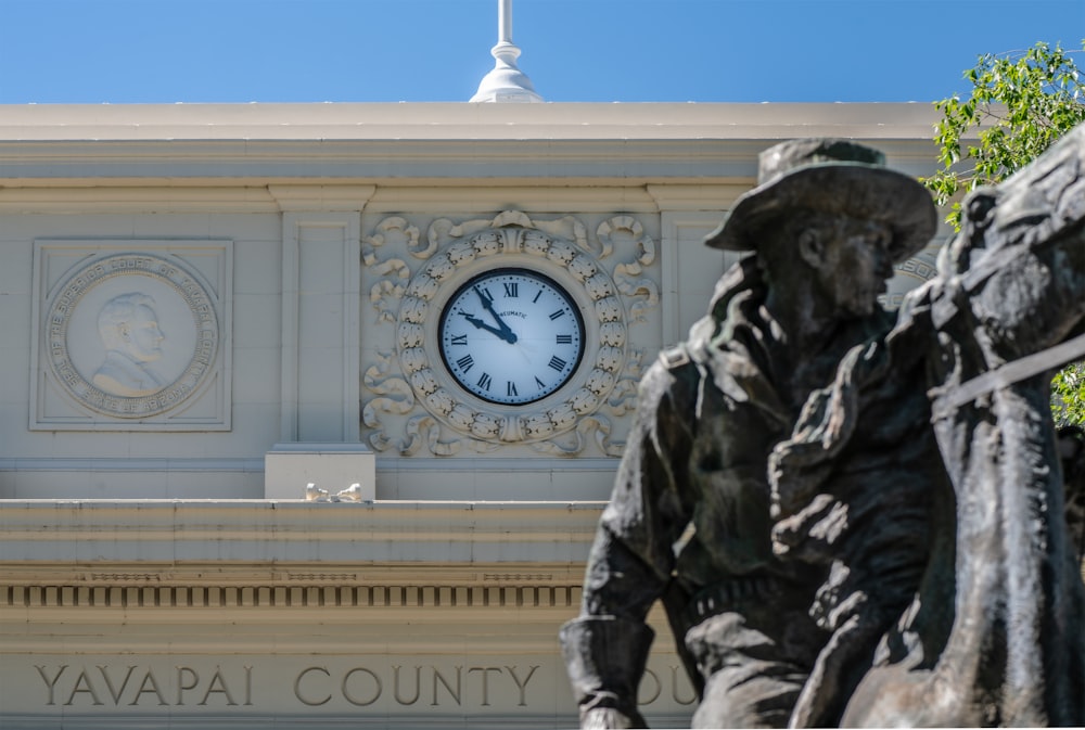 a clock on the side of a building with statues in front of it