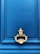Photo of a door knocker in royal blue uniform standing confidently on a doorstep with golden accents.
