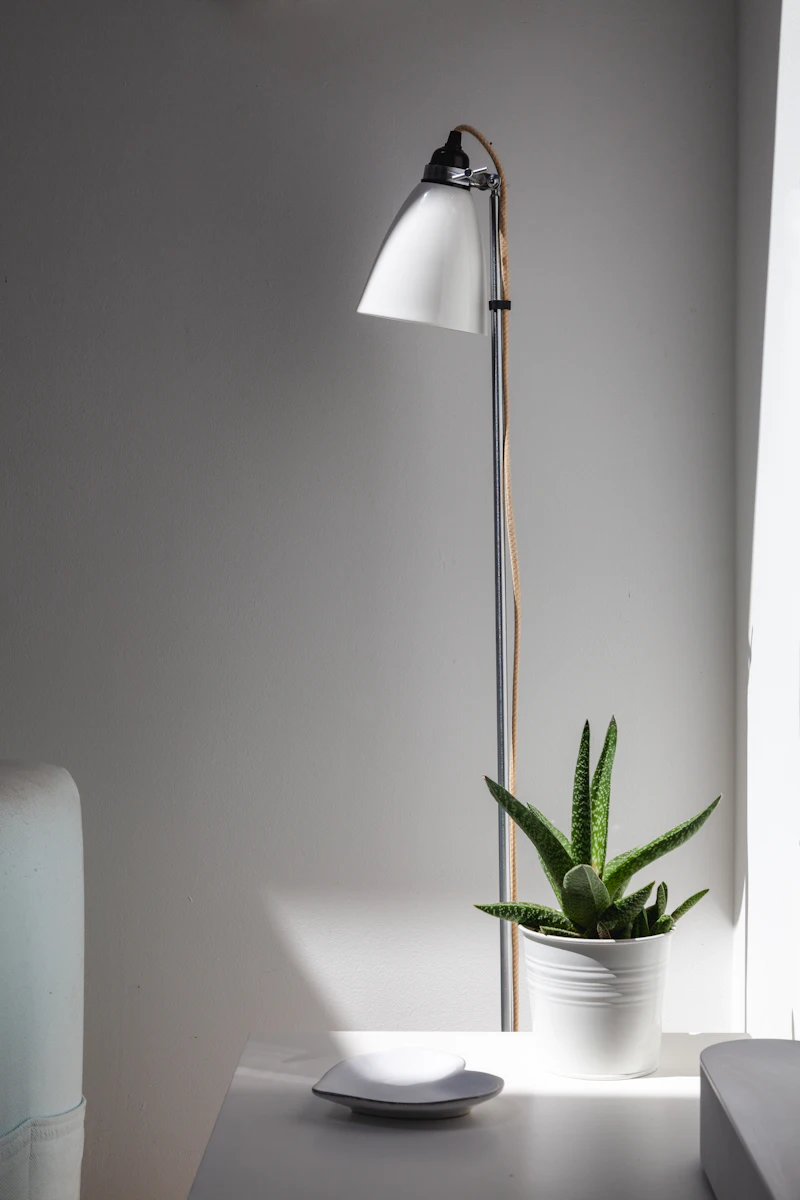 Lámpara de mesa de cerámica sobre una mesa blanca junto a una planta