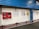 A tiled wall featuring a red fire equipment box and several informational posters. The setting appears to be industrial or public, with blue corrugated metal siding above the wall and a chain barrier in the foreground.