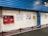 A tiled wall featuring a red fire equipment box and several informational posters. The setting appears to be industrial or public, with blue corrugated metal siding above the wall and a chain barrier in the foreground.
