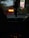 The scene takes place inside a car with a GPS on the dashboard. Dim lighting outside suggests evening or night, complementing the glow of the electronic displays. Hanging from the rear-view mirror are assorted objects.