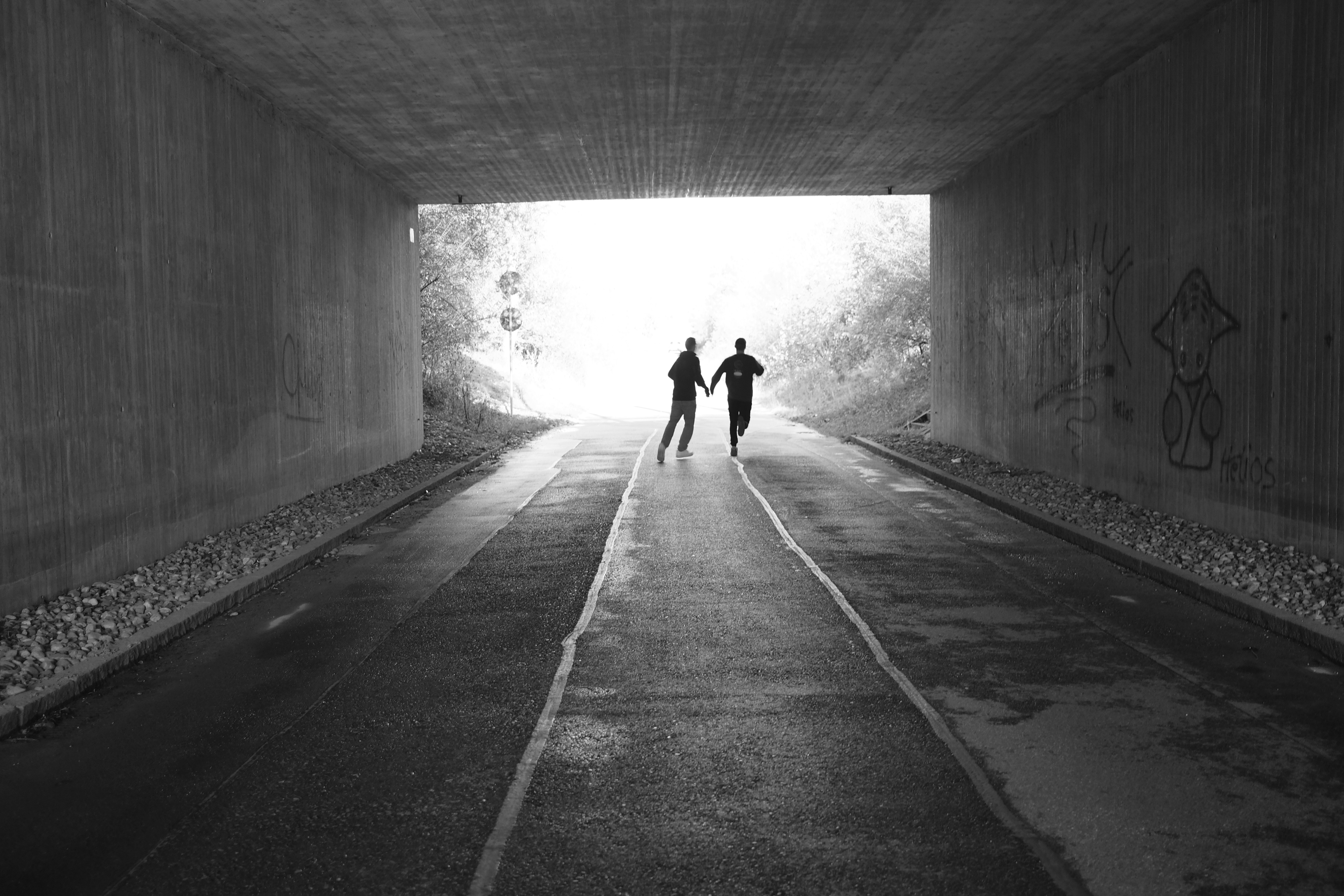 Silhouette running through dark tunnel with a single blinding light source ahead