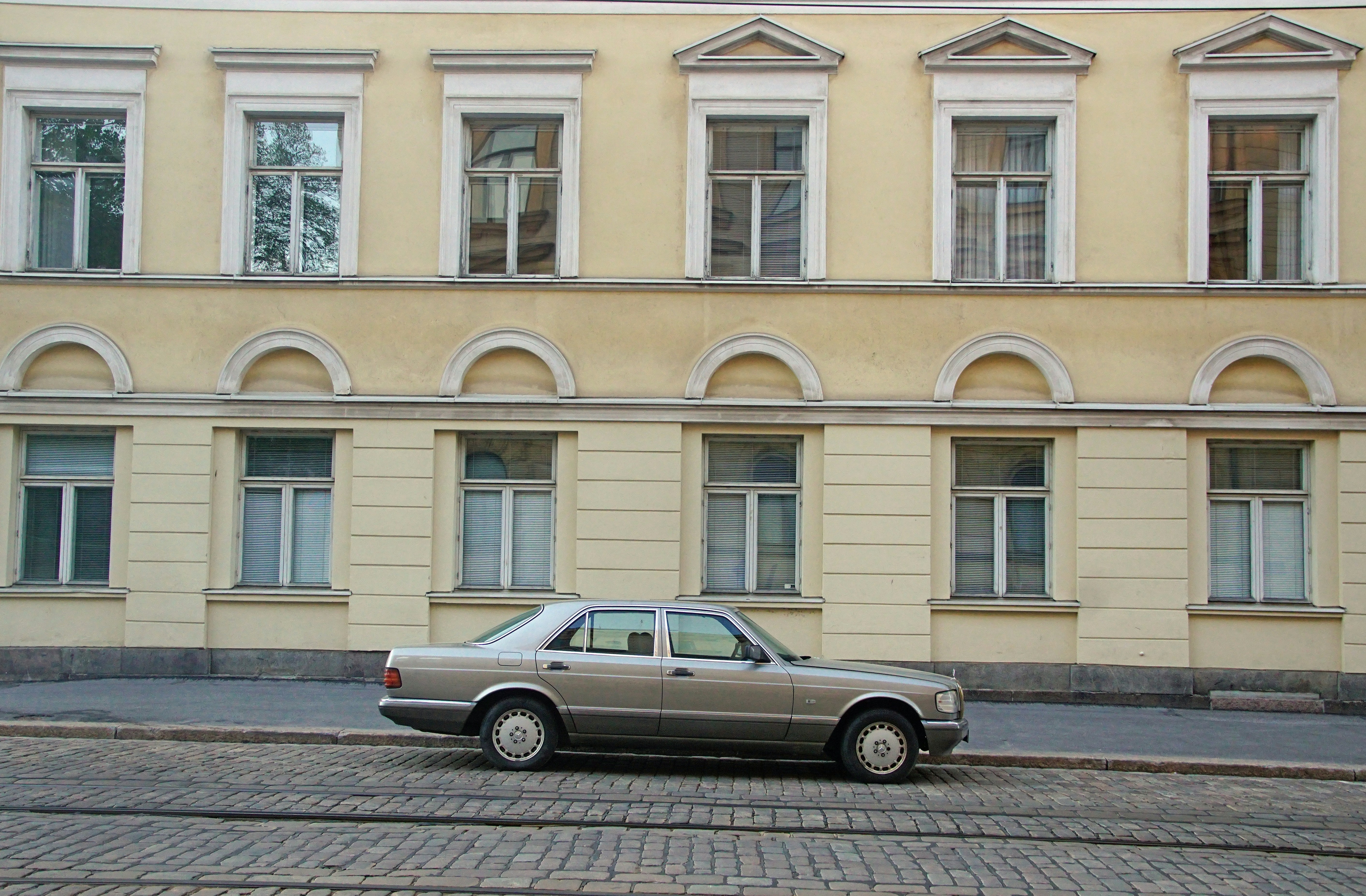 A 1980s gray luxury car, a Mercedes Benz, in front of a fairly old building in Helsinki, Finland.