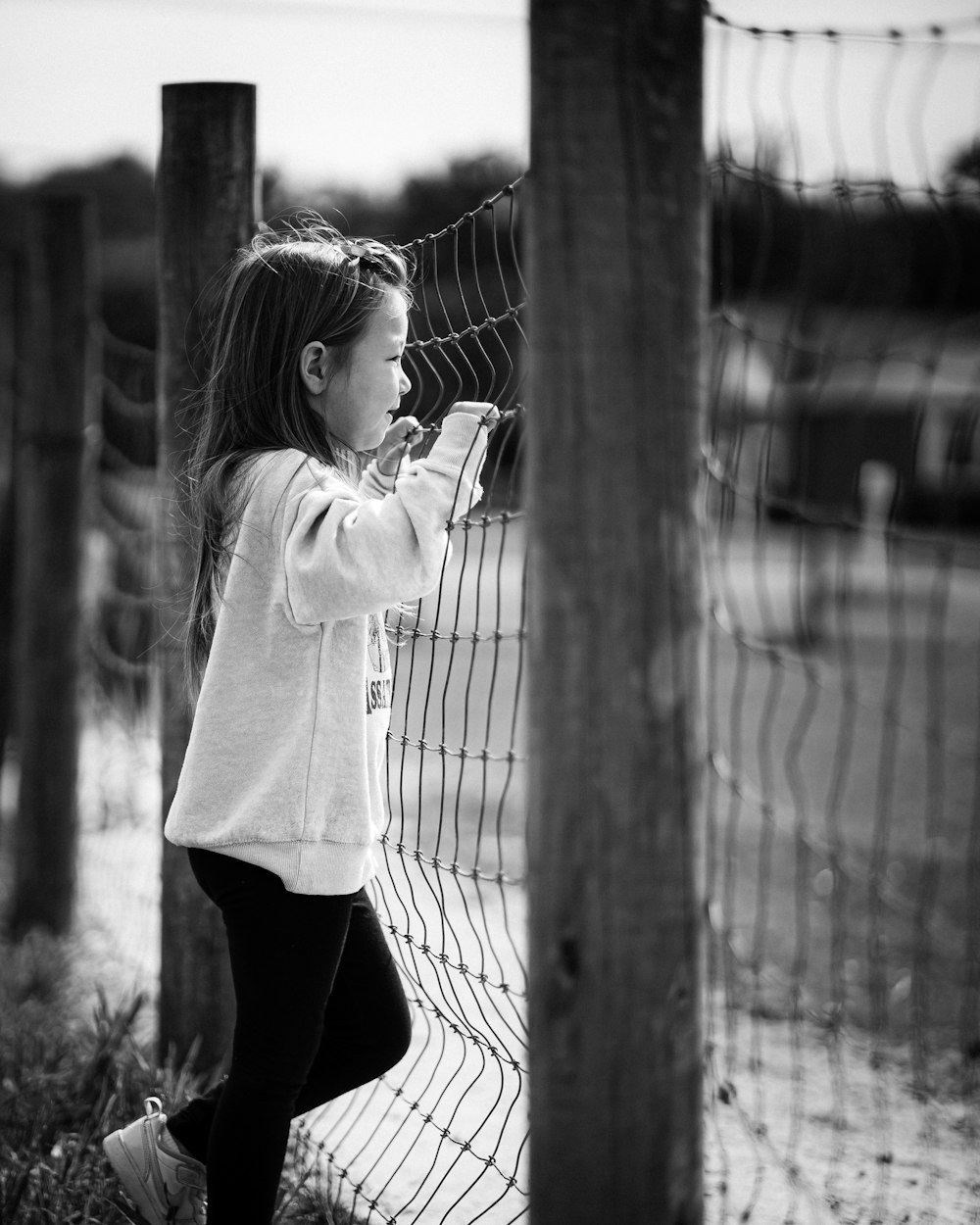 a little girl standing next to a fence