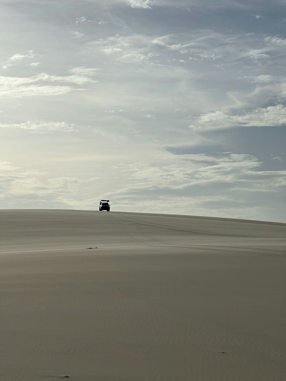 a truck driving across a sandy field under a cloudy sky