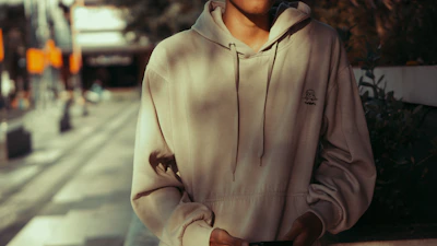 A cozy model wearing a soft beige hoodie from Velora, standing against a minimalist urban backdrop.