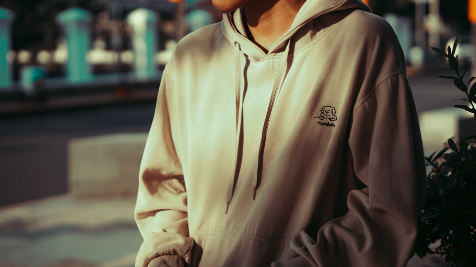 Detail hoodie krem dikenakan di luar ruangan saat sore