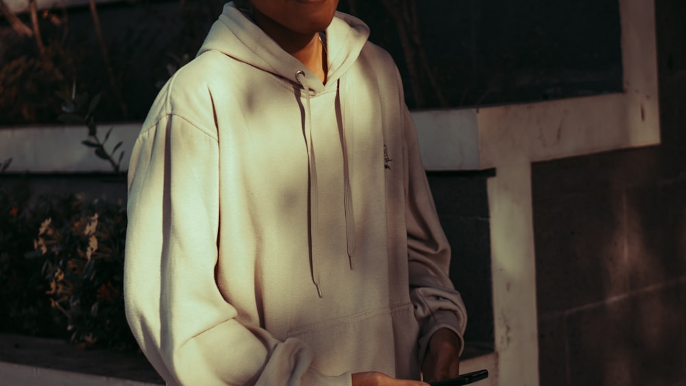 a man in a white hoodie holding a cell phone